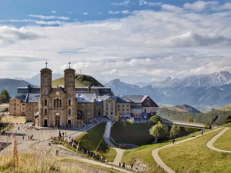 A large church with double towers set in a grassy area with a backdrop of snowy mountains