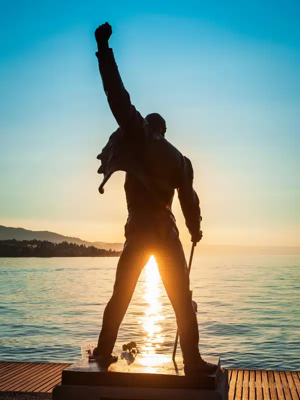 Statue of a man with one hand in the air and the other holding a cane, in front of a lack at sunset