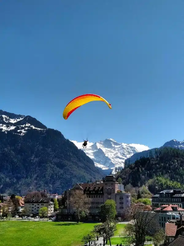 Red and yellow tandem paraglider in front of a Swiss town