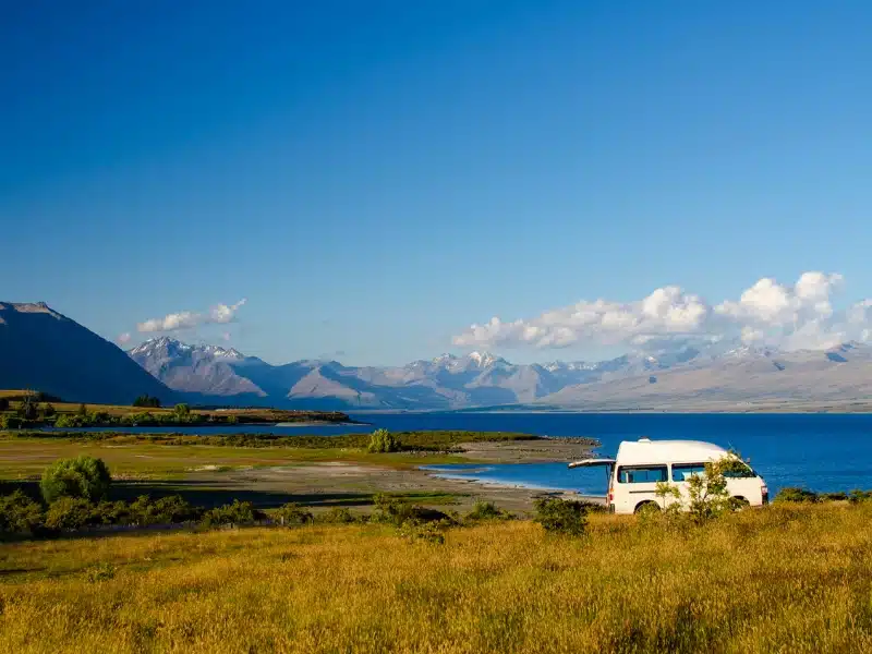 white camper van parked by a blue lake with mountains in the background