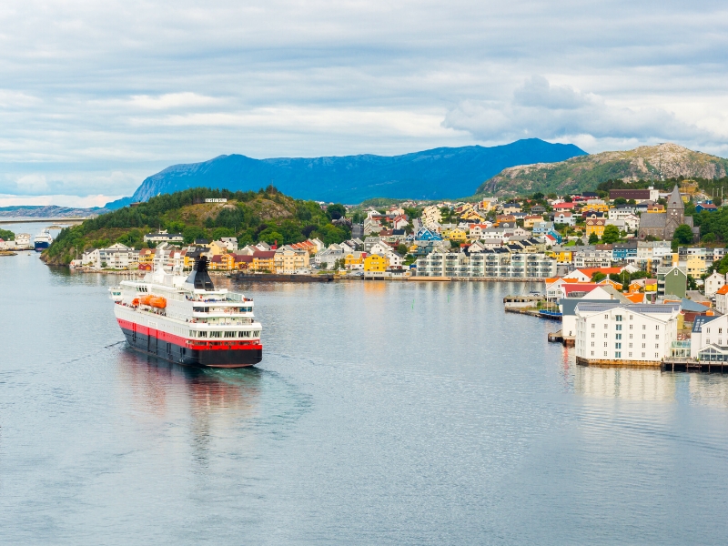 A red white and blue ferry in a harbour of colorful houses, backed by mountains