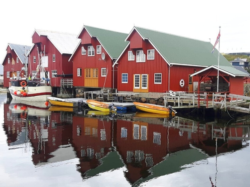 Red clapboard houses by the water, with small yellow boats moored in front.