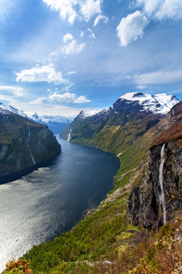A sweeping Norwegian fjord with almost vertical snow capped mountain walls on either side.