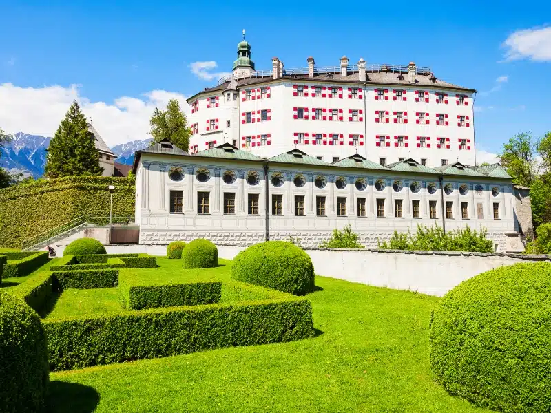 white bulding with red windows surrounded by lush gardens and hedging