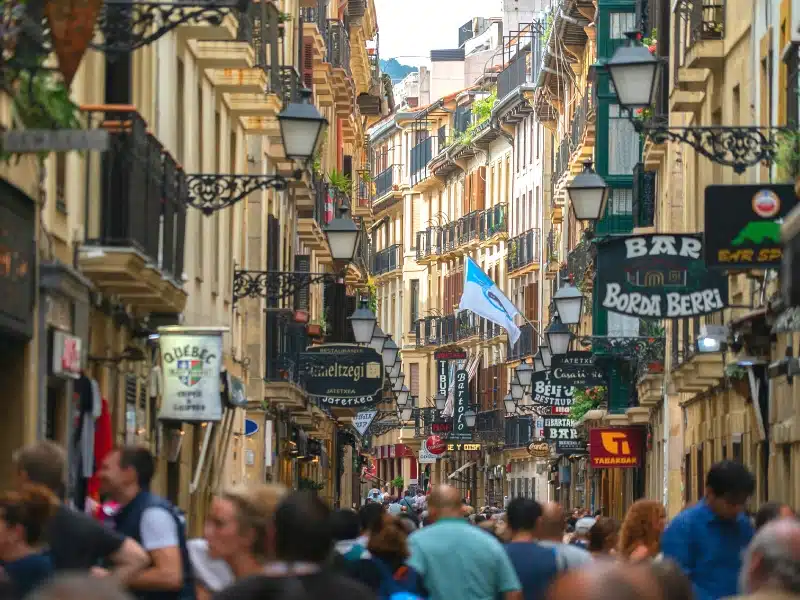 A busy Spanish pedestrian street with five and six story historic buildings on either side.