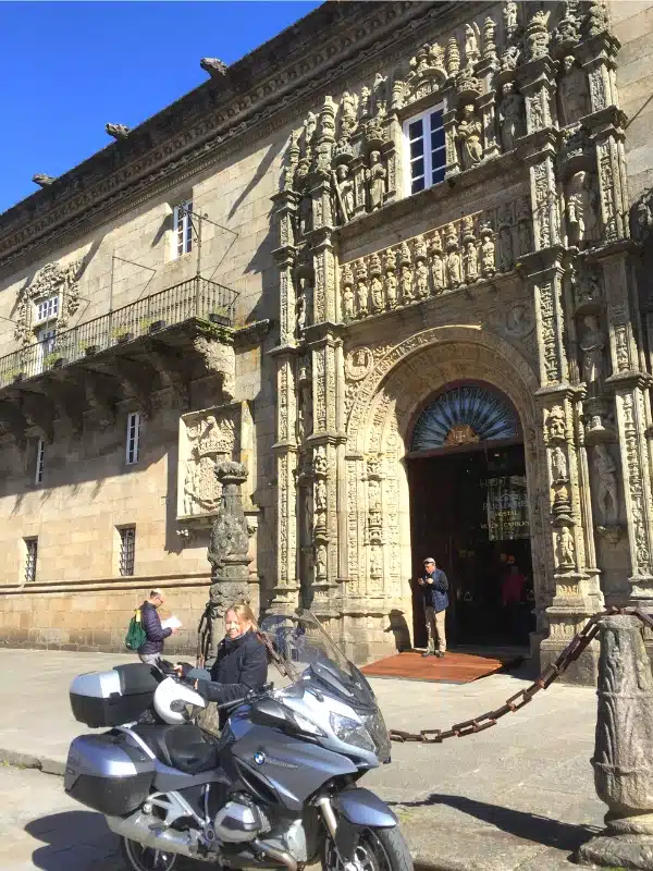 A woman by a large motorbike outside an historic city centre hotel in Spain