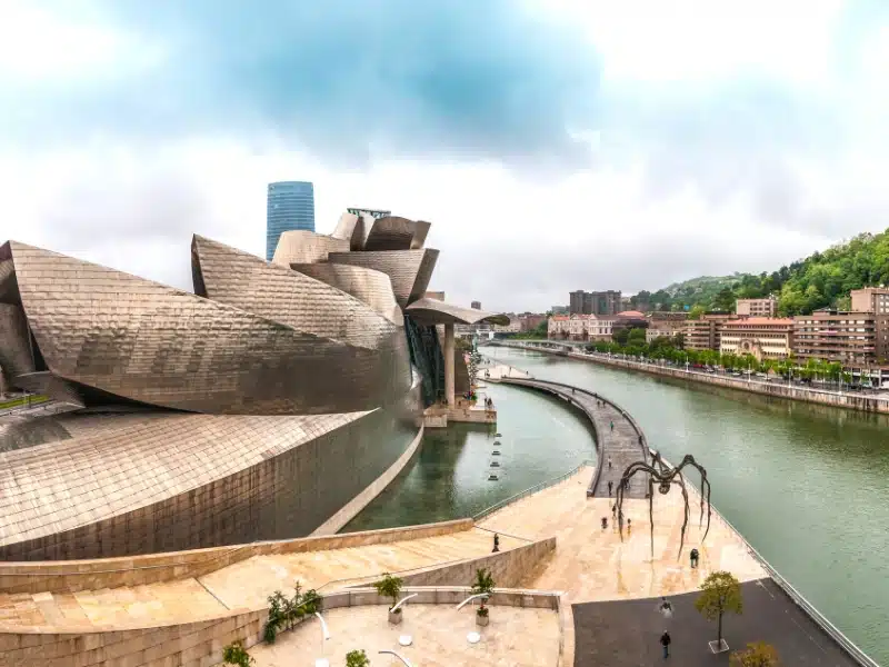 a contemporary building on a riverside with a spider sculpture outside