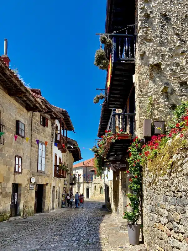 A cobbled street lined b stone buildings and balconies with red flowers