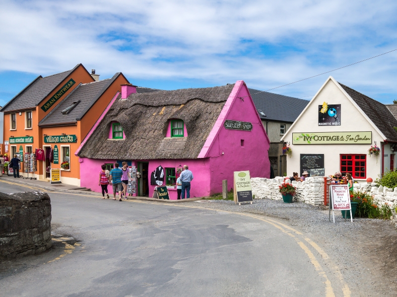 bright pink and orange houses and shops by a road through a small Irish village