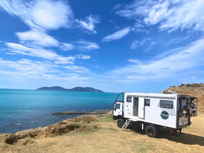 white overland truck parking on a grassy cliff overlooking a turquoise blue sea