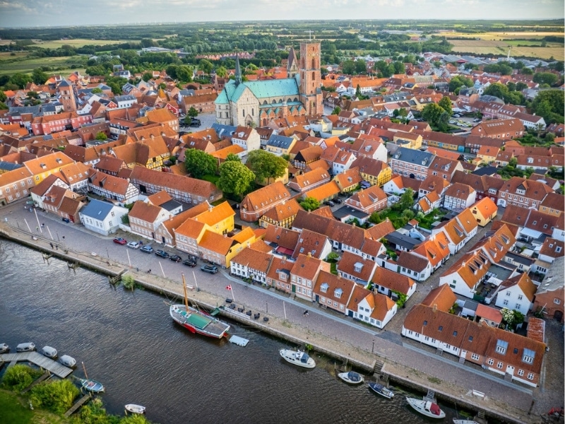 Aerial view of historic town Ribe with majestic Ribe cathedral, red-roofed buildings and boats docked along the riverside, set against lush, green landscape, south-west Jutland, Denmark