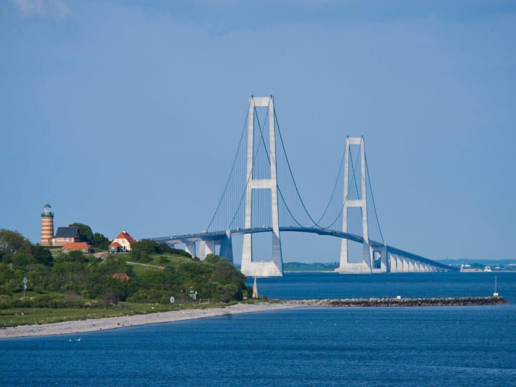 Modern large bridge over blue water with high arches and a lighthouse in the foreground