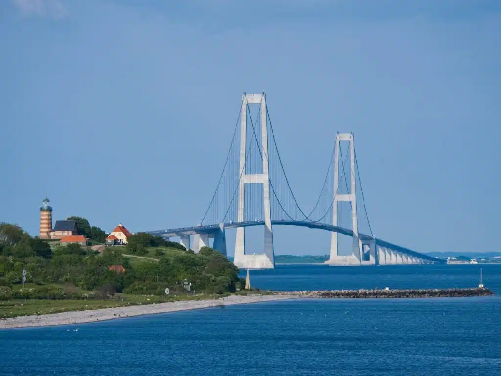 Modern large bridge over blue water with high arches and a lighthouse in the foreground