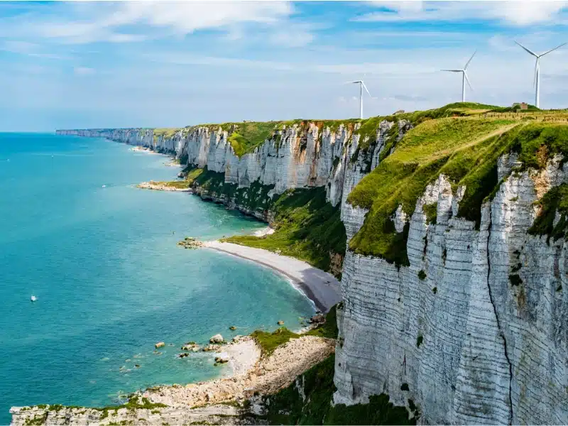 White cliffs topped with grass and wind turbines overlooking white sandy beaches and turquoise sea
