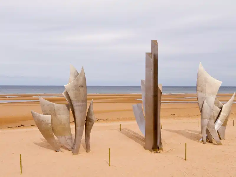 modenr metal sculpture on a large sandy beach with sea in the distance