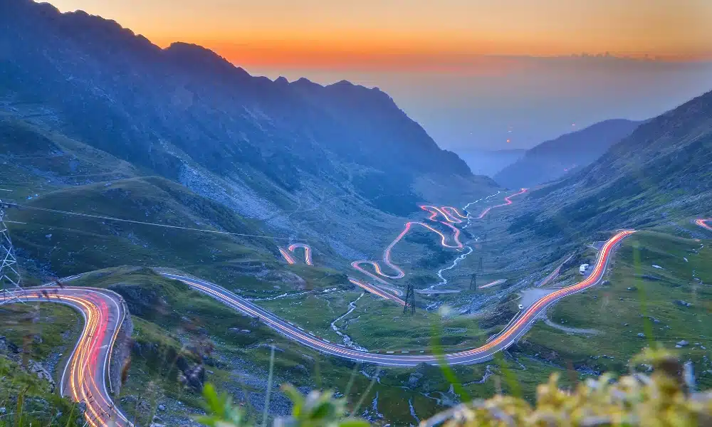 mountain road at sunset with car lights glowing in the dusk