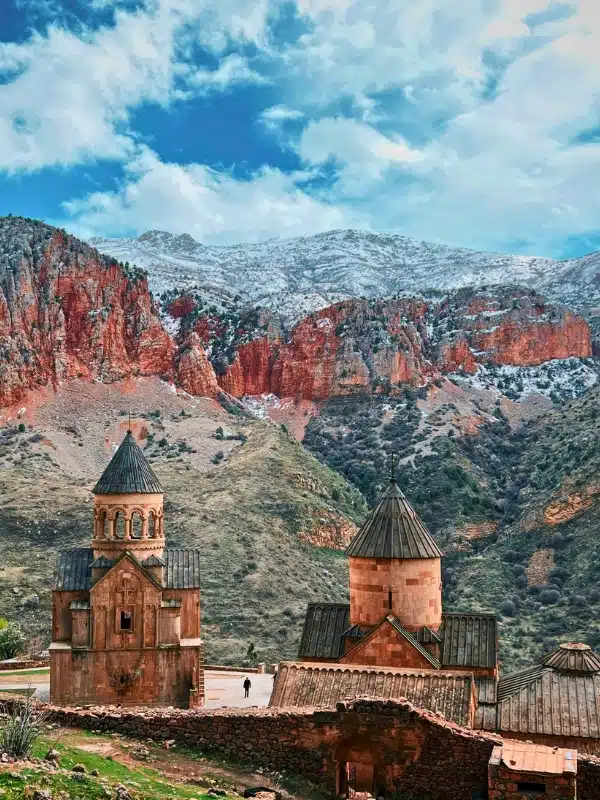 Rose colored stone monastery buildings with snowy mountains in the distance