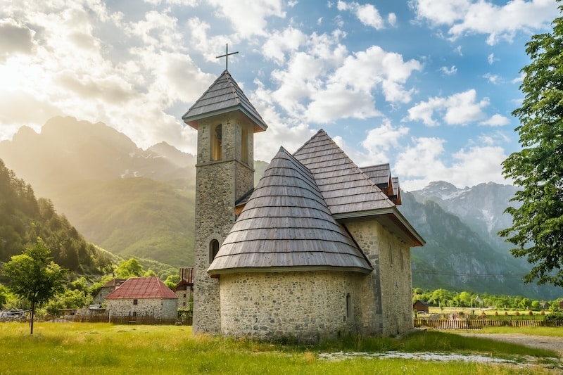 small stone and wooden church surrounded by houses and mountains