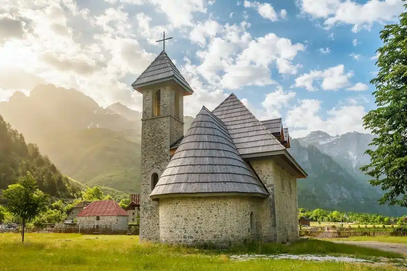 small stone and wooden church surrounded by houses and mountains