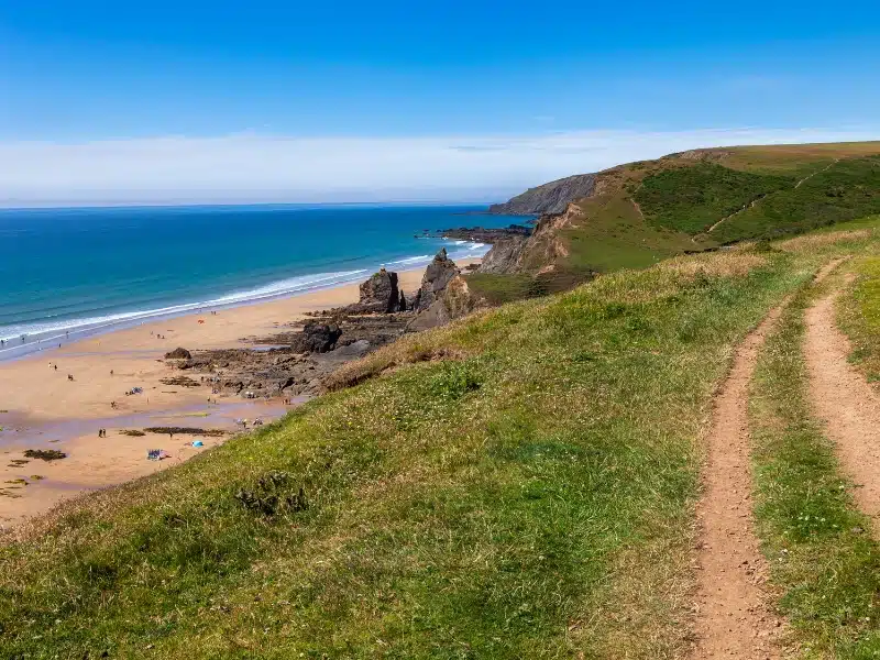 grassy path above a long sandy beach backed by rocks