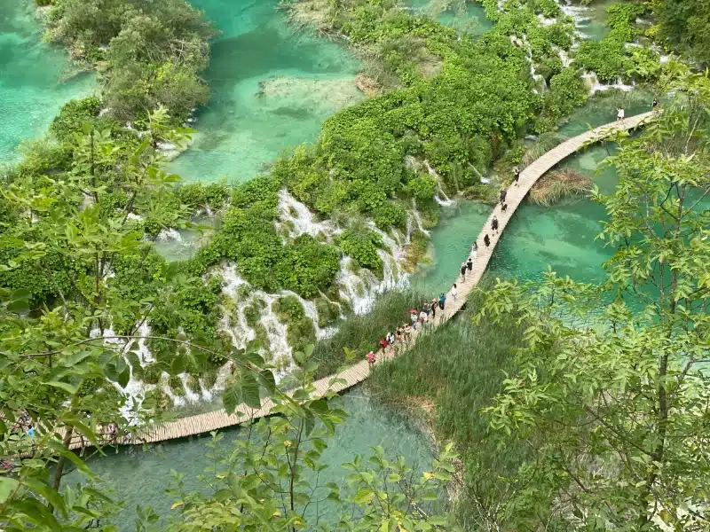 wooden boardwalk over a green lake with multiple waterfalls
