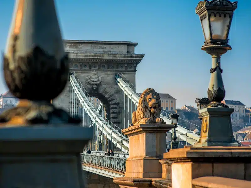An image of the entry to a suspension bridge, with lion statues guarding the entry