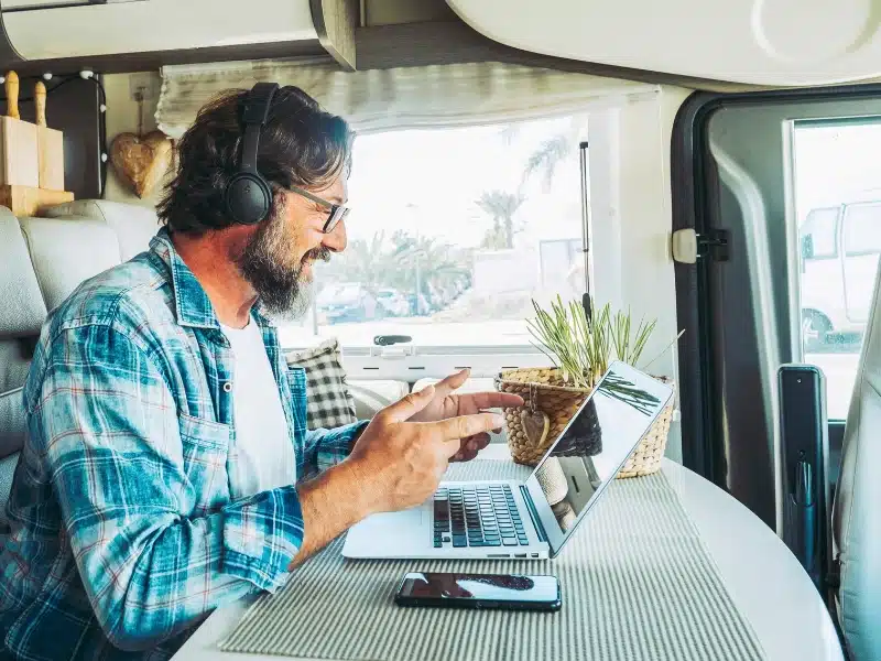 Modern online worker smart working digital nomad lifestyle in camper van. Travel people and technology. Alternative business job. Content creator influencer. Man using computer laptop and connection