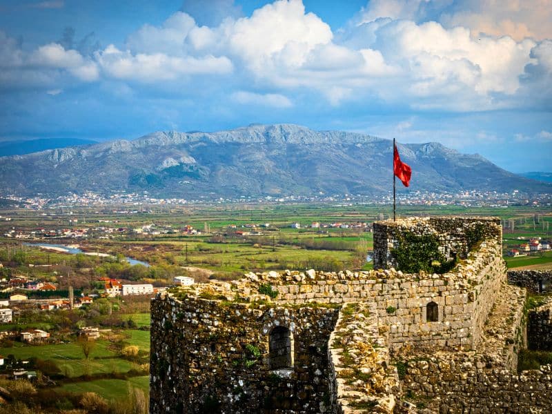 A vibrant red flag is waving proudly atop the remnants of an ancient, crumbling castle that has seen better days
