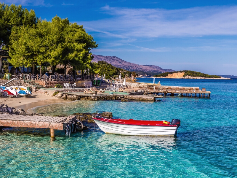 red and white boat tied to a wooden pier jutting into a clear turquoise sea