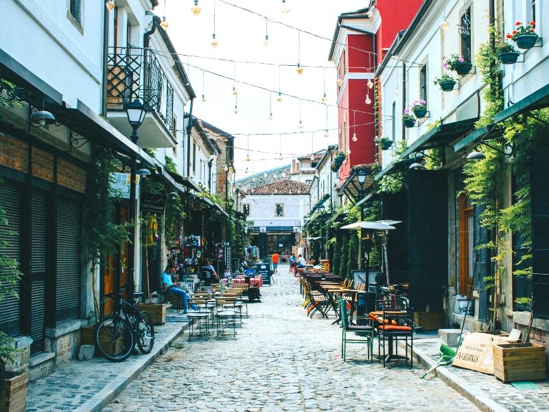 cobbled street with fairly lights stung above and tables and chairs set ouy