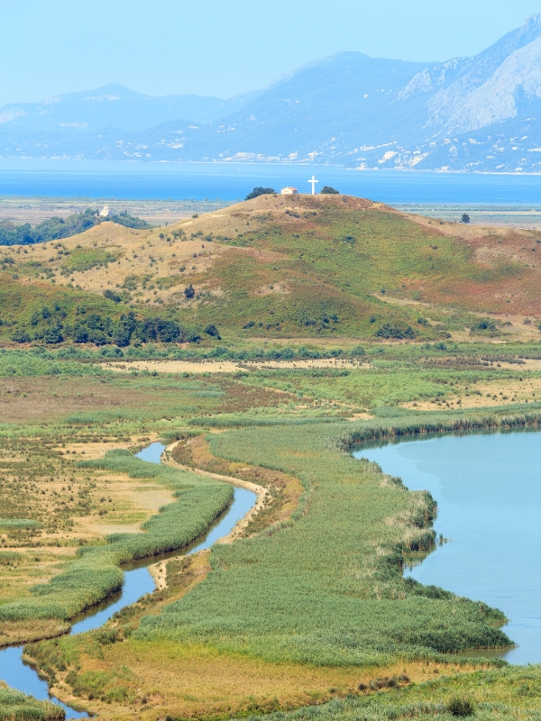 small hill with a cross on top surrounded by large body of water