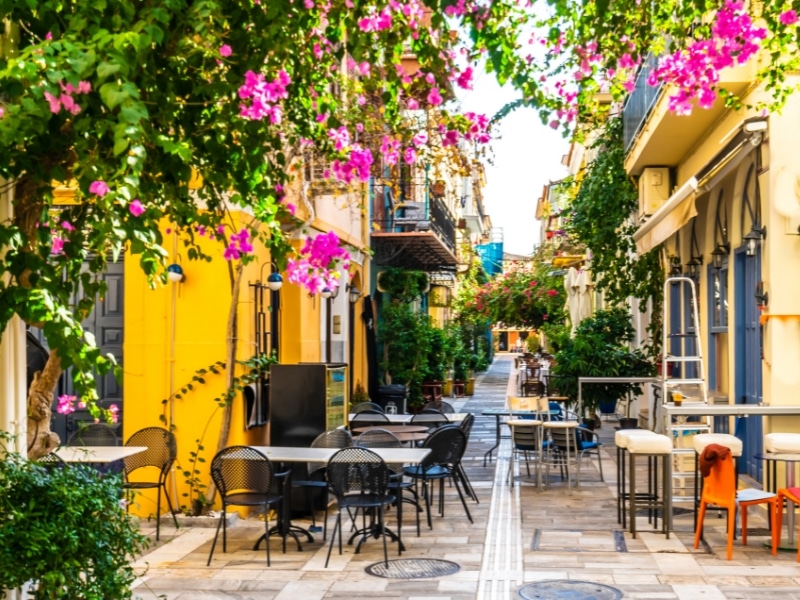 pink flowers again a street of yellow and blue buildings with chairs and tables outside