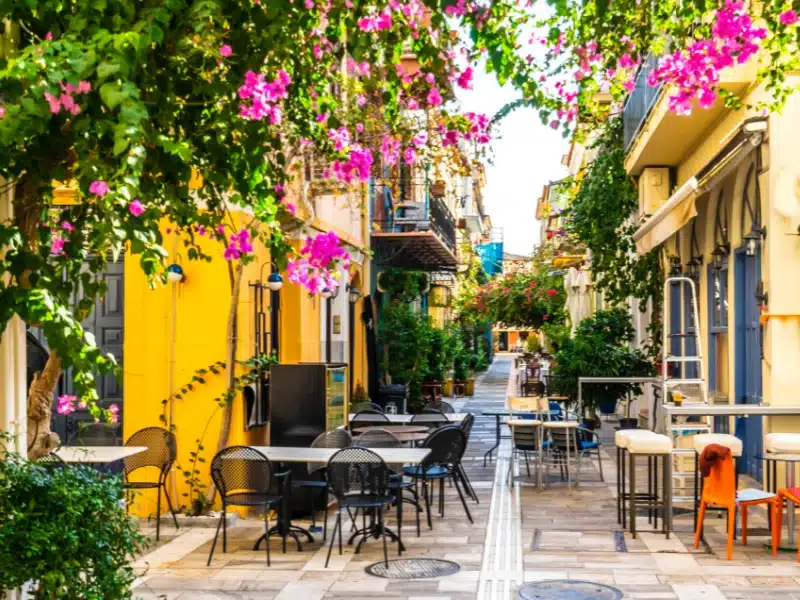 pink flowers again a street of yellow and blue buildings with chairs and tables outside