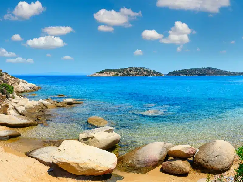 Bright blue sea with large smooth rocks in foreground and islands out to sea