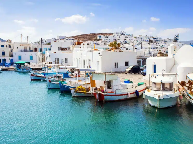 colorful fishing boats moored in front of white and blue houese rising on a hill