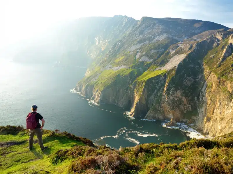 Man standing admiring tall cliffs aboce a foaming sea