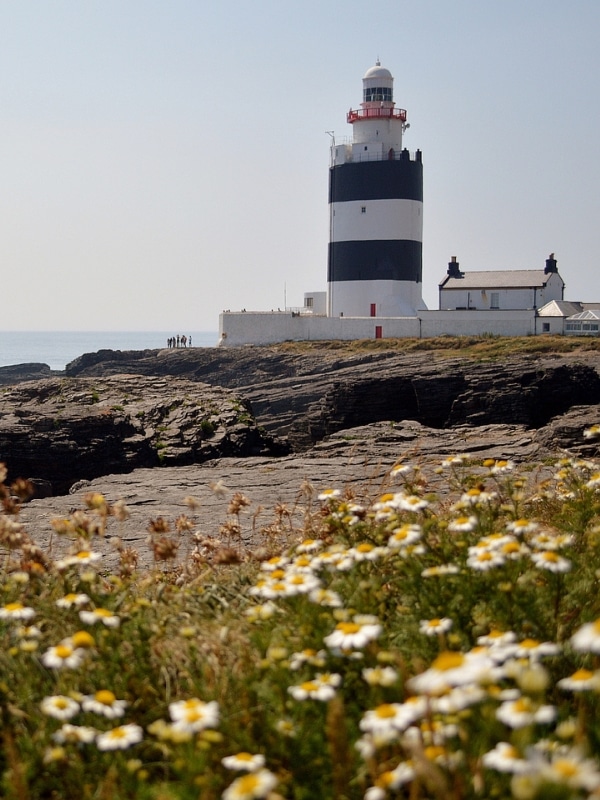 Blue and white striped lighthouse next to a small white house with the sea in the background