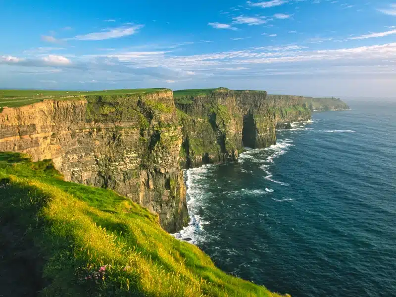 Tall granite cliffs above steel blue sea topped with grass 