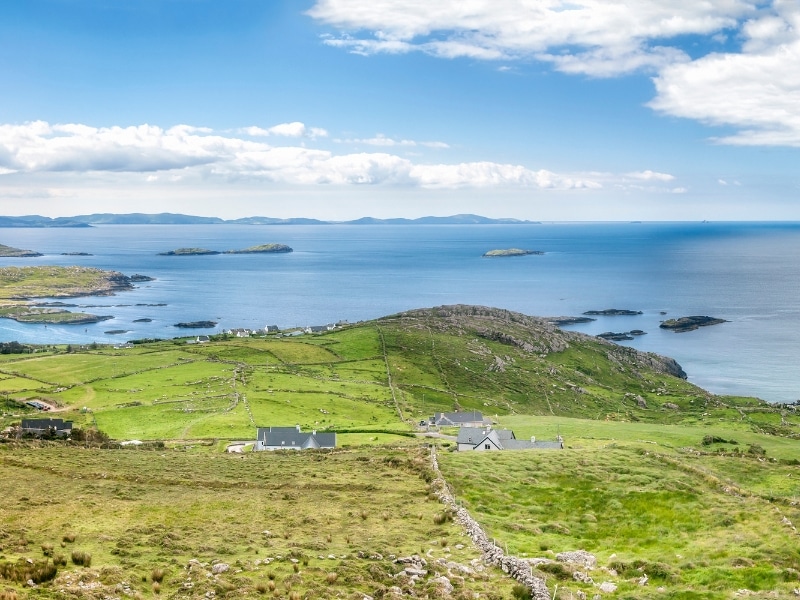 View over rolling green fields to the ocean with a few houses dotted about