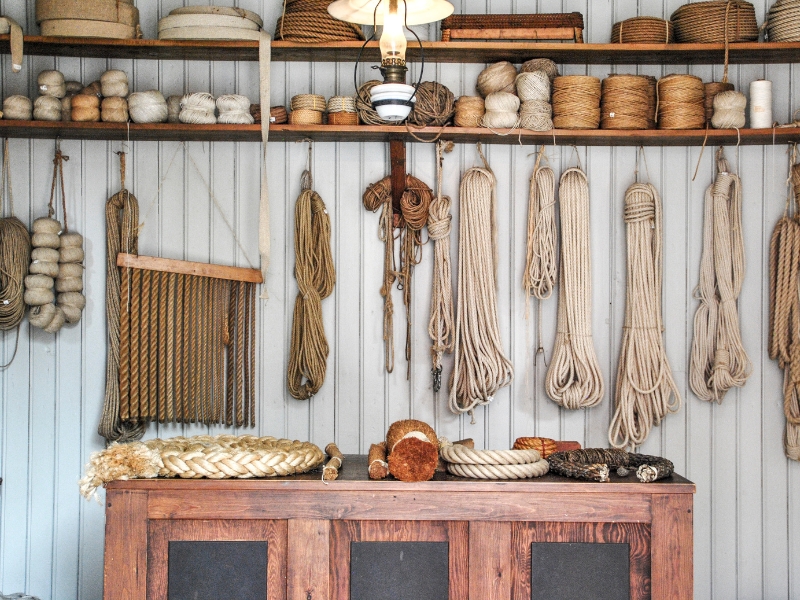 collection of string and rope of varying widths and lengths hanging in a room lined with wood