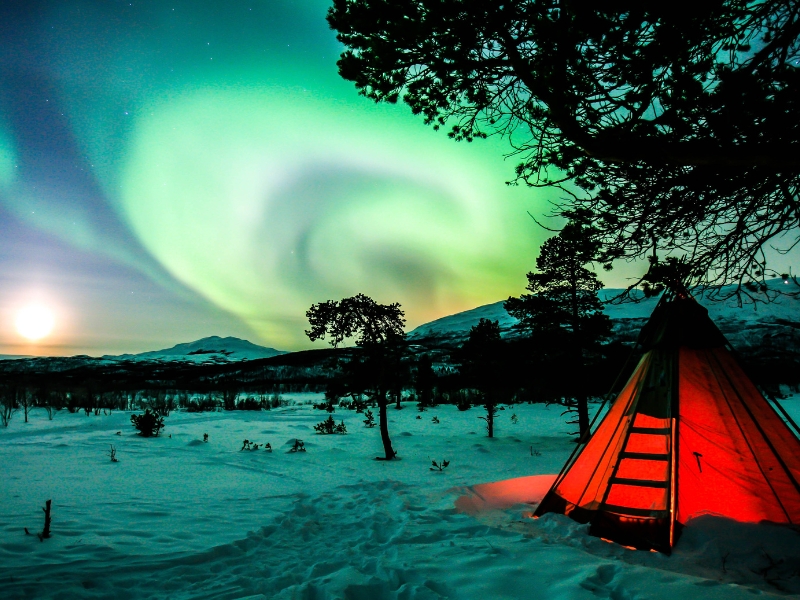the northern lights above a field covered in snow with a red tent lit from inside
