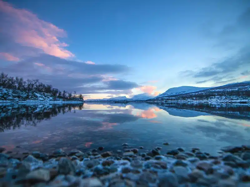 a clear lake surrouned by trees and snow capped mountains