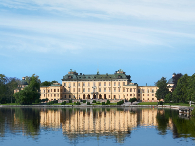 gradn crem colored palace with a copper roof and a lake in front