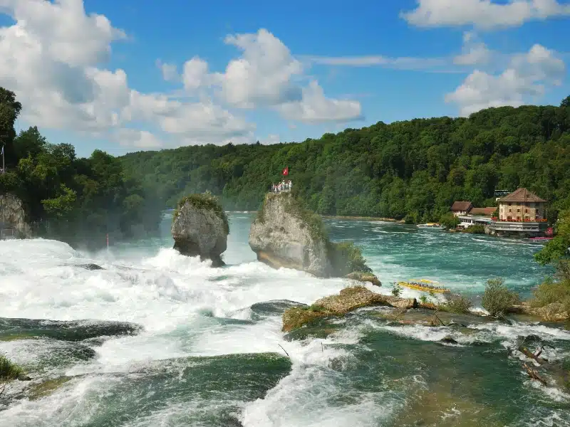 Large and wide waterfall with a rock in the middle flying the Swiss flag