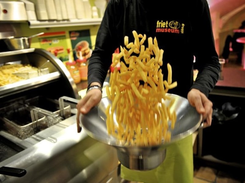 person shaking a large metal pan of frites