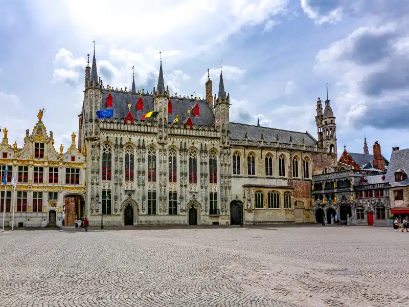 historic buildings flying the Belgian and EU flags in a square in Bruges
