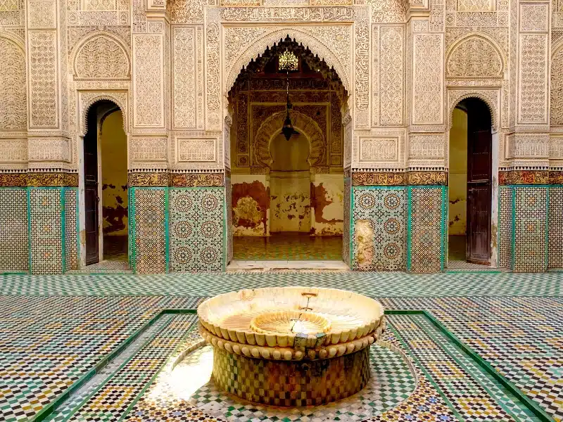 Ornate Moroccan palace room with intricate mosaic tiles and a central water fountain