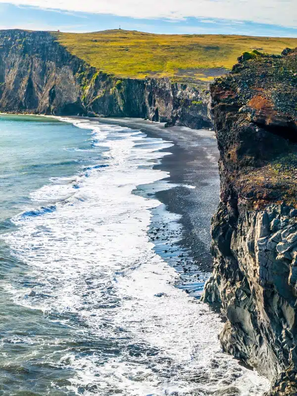 Black sand beach with blue sea backed by grassy cliffs