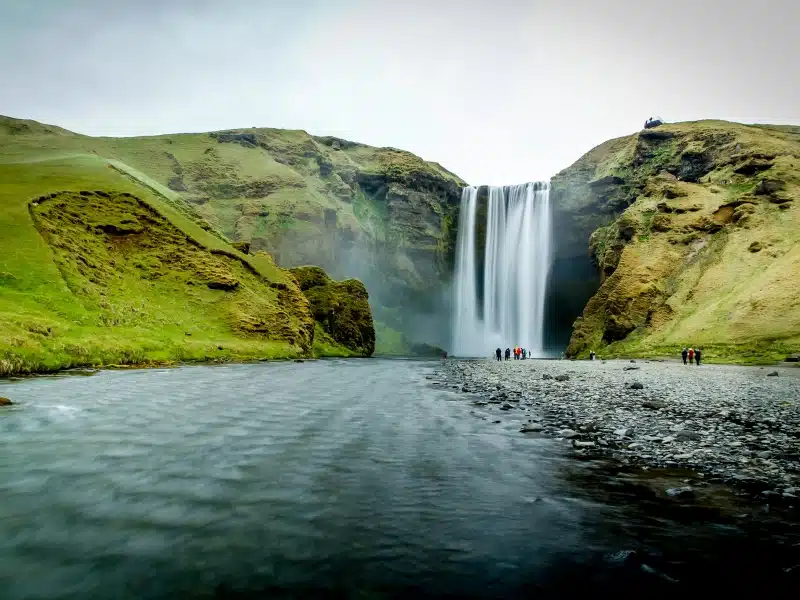 Tall waterfall cascading down green cliffs with people watching