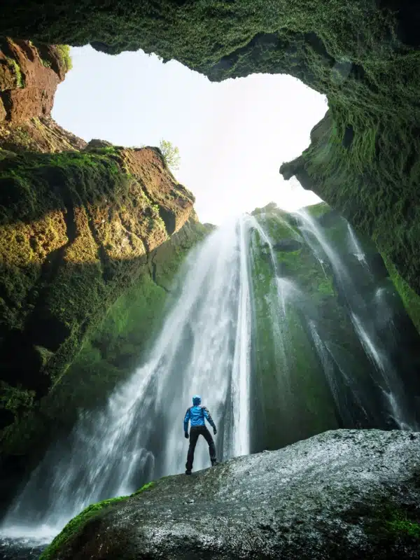 waterfall coming through canyon with man standing underneath